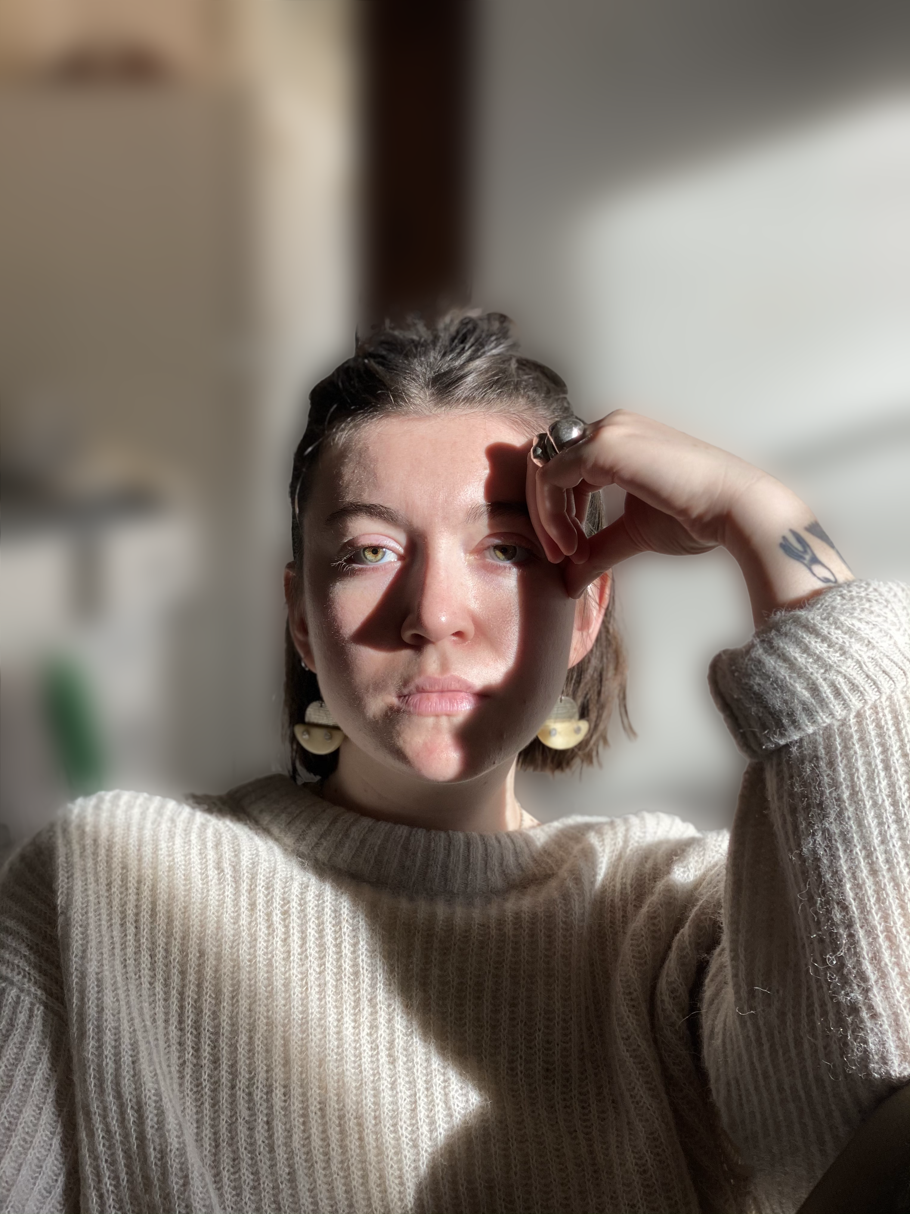 Photo of a woman with brown hair wearing earrings and a cream colored sweater holding her hand to her forehand